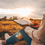Person hat eine geöffnete Bibel auf dem Schoß in der Natur