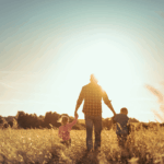 Mann geht mit zwei Kindern an der Hand über ein Feld