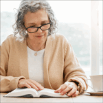 Ältere Dame mit grauen Haaren und einer Brille liest ein Buch